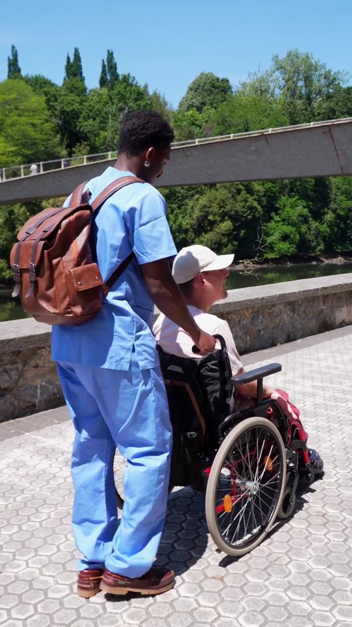 Assistente che spinge un uomo anziano su sedia a rotelle lungo la riva del fiume