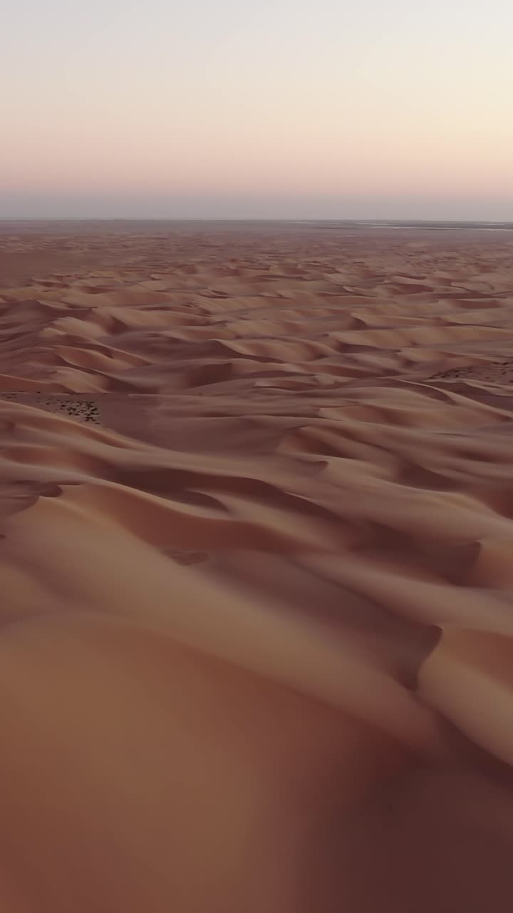 Splendida vista aerea di un vasto paesaggio desertico. Impressionanti dune di sabbia che si estendono fino all'orizzonte sotto un cielo al tramonto dai colori pastello nel Sahara
