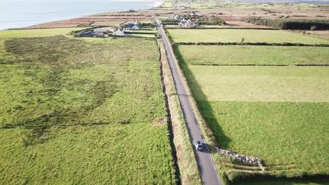 aerial-view-of-meadows-and-a-road-with-a-car-driving-in-Connemara,-Ireland