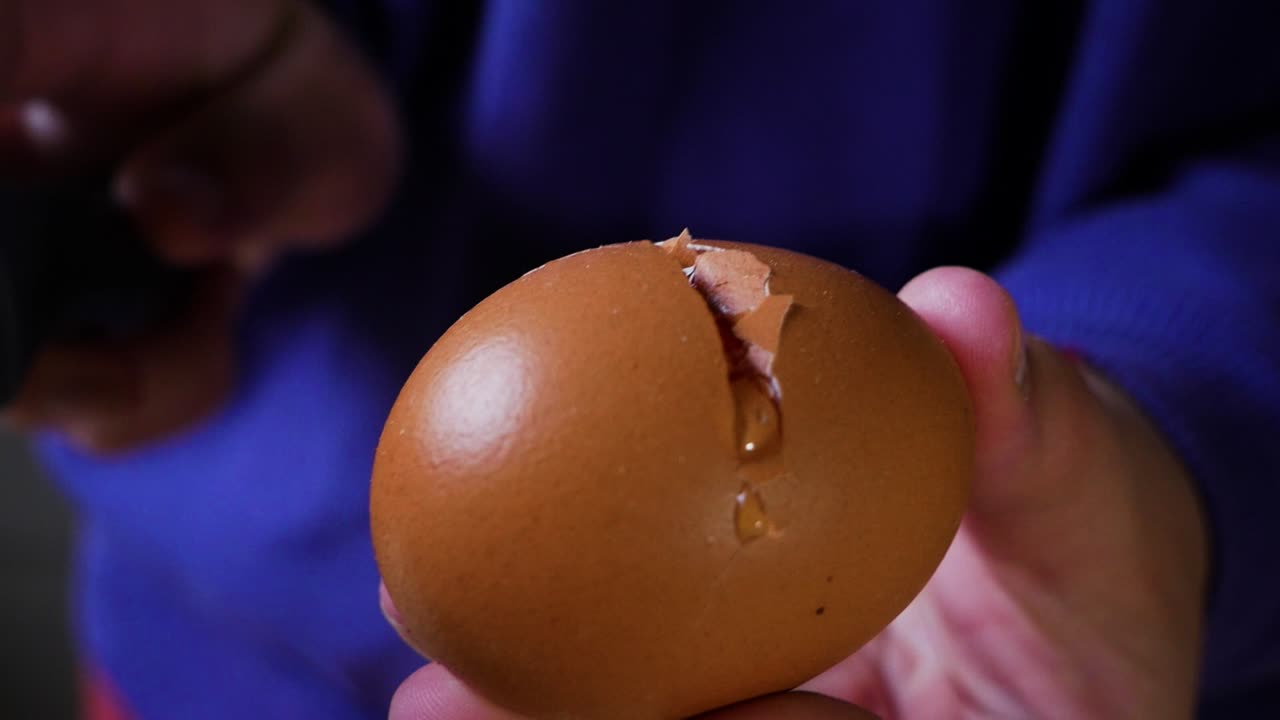 Female home cook cracks egg using knife while holding egg in her hands