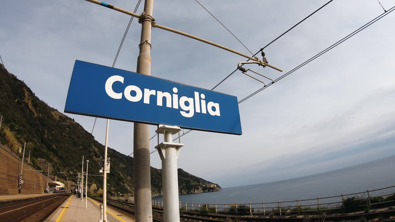 cartel de la ciudad de corniglia en una estación de tren filmada durante el día con un bonito cielo nublado