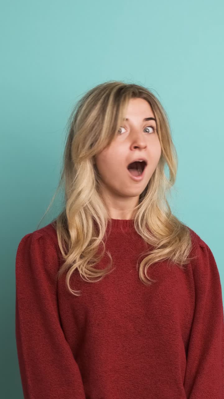 Stunned young woman with opened mouth in blue studio