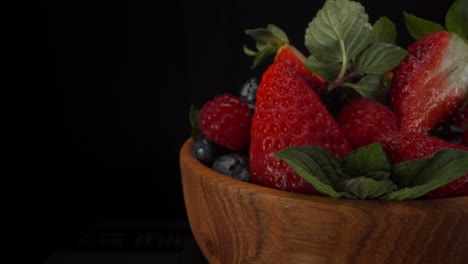 incredibly juicy rotating forest fruits in a wooden bowl with black background, strawberries, blueberries, raspberries, healthy fruits, 4k shot with copy space