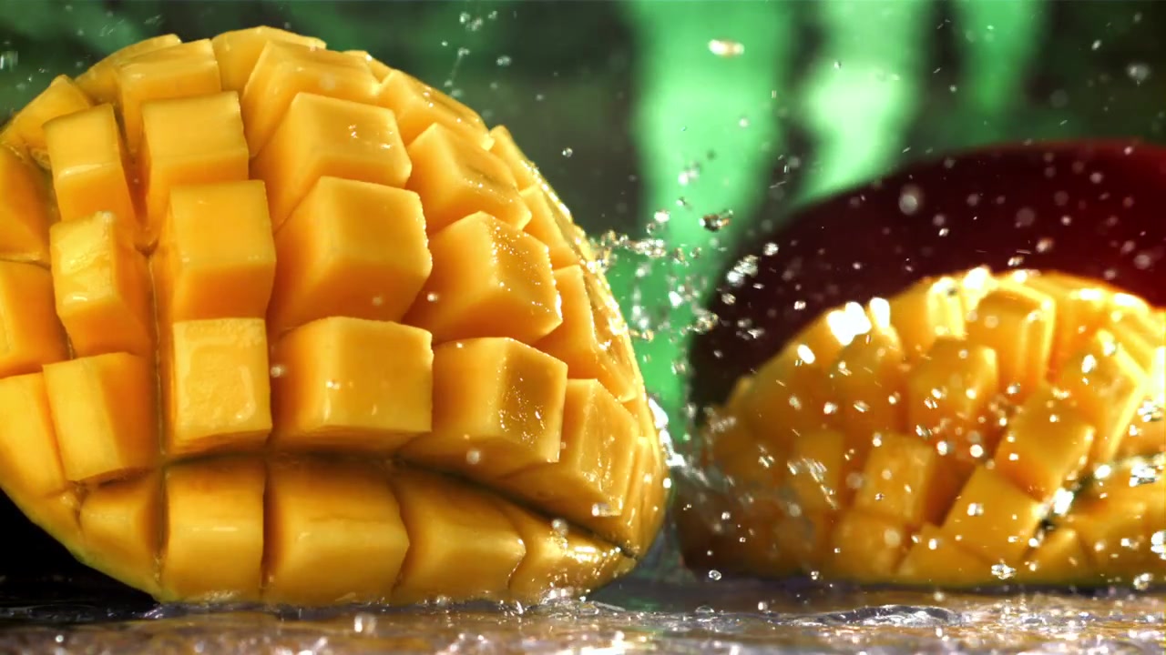 Schizzi d'acqua al rallentatore su metà di mango appena tagliate.