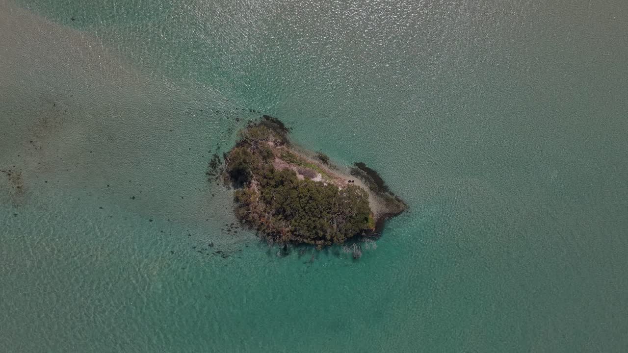 Drone top down rotates over calm clear waters near Pirrita Island, gentle morning waves and reef structure, abstract panoramic