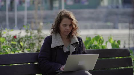 mujer de mediana edad enfocada usando una computadora portátil al aire libre