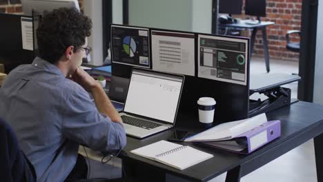 Caucasian man sitting at desk watching coding data processing on laptop and computer screen