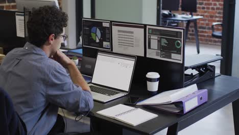 caucasian man sitting at desk watching coding data processing on laptop and computer screen