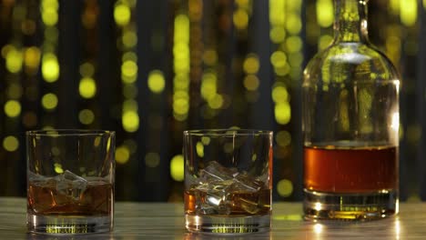 barman popycha, kładzie dwie szklanki ze złotą whisky, koniakiem lub brandy z kostkami lodu na drewniany stół