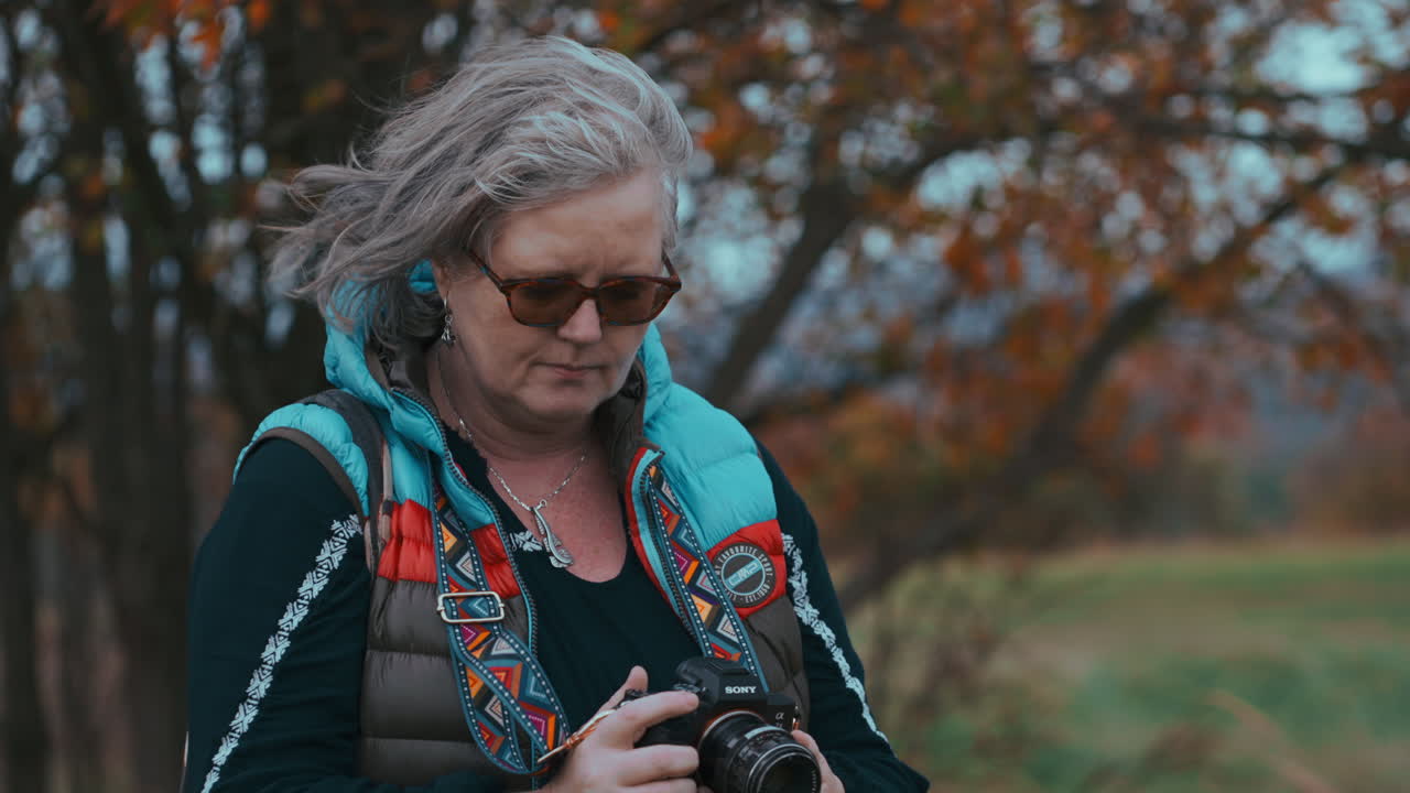 Close up shot of a woman taking pictures with her camera surrounded by beautiful colourful autumn nature during a cold and windy day in slow motion