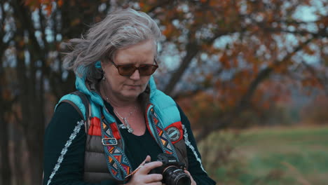 Close-up-shot-of-a-woman-taking-pictures-with-her-camera-surrounded-by-beautiful-colourful-autumn-nature-during-a-cold-and-windy-day-in-slow-motion