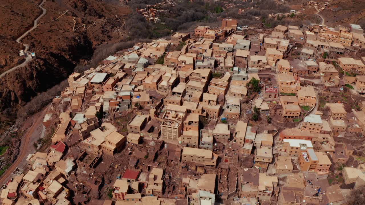Top down aerial drone shot over remote rural Moroccan village on the Atlas Mountains. Camera moving forward showing the houses' rooftops.