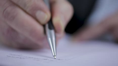 primer plano de una persona escribiendo en papel, enfoque en la mano y el bolígrafo, fondo borroso