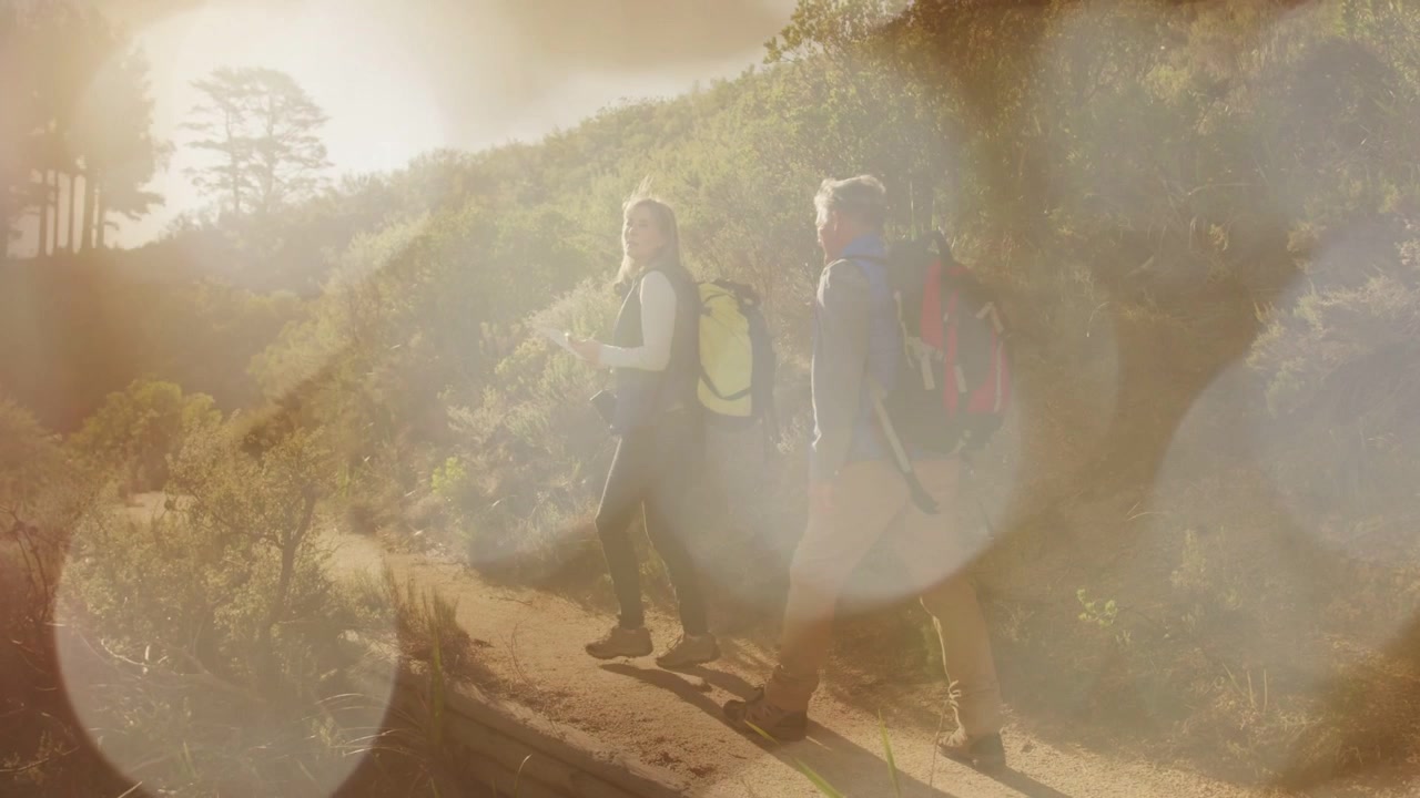 Führender Wanderer tritt voran, Begleiter folgt, Rucksäcke und Lichtreflex verdecken teilweise Wanderer auf einer Wanderung.