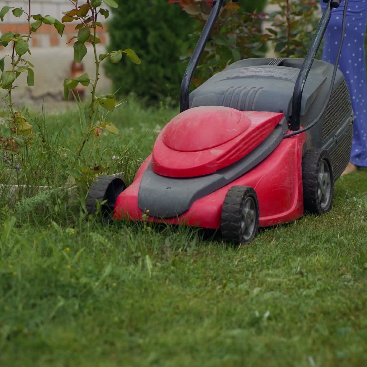 Woman running with a lawn mower in the garden. Close-up