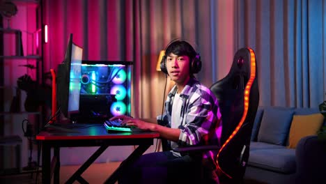 un adolescente asiático sonriendo a la cámara mientras juega a videojuegos en la computadora