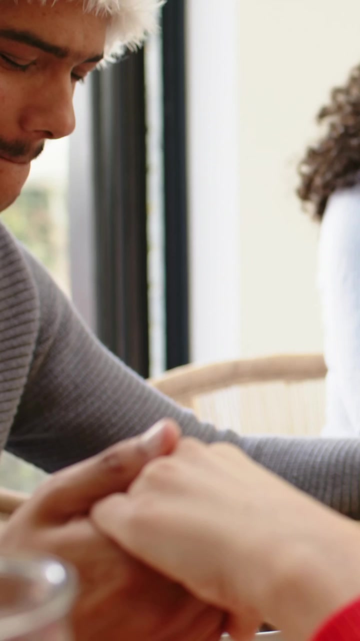 Vertical video: Man in grey sweater hat holding, rubbing hand at table by window close-up, soothing