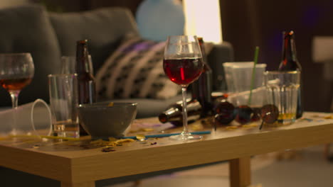 close up of messy lounge or living room with table covered with empty wine glasses and beer bottles after house party 2