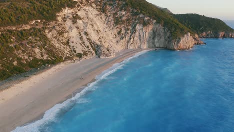 aerial coast revealingn footage of beautiful milos beach of lefkada, ionian island, greece. sunset golden sunlight and pristine waves breaking the turquoise blue sea on the shore