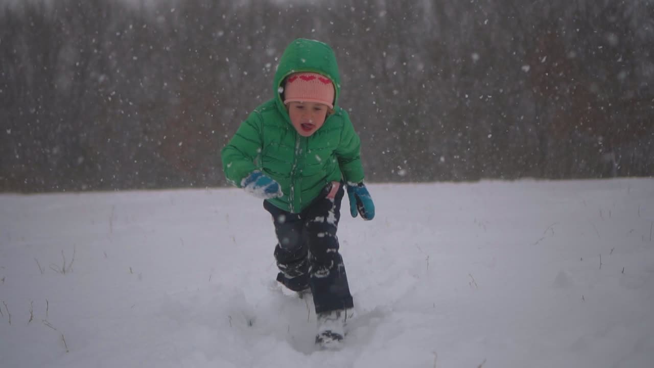 niño corre y se sumerge en la nieve, luego sonríe a la cámara, nieve cayendo a cámara lenta