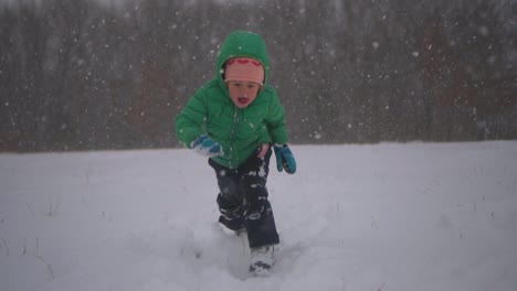 young boy runs and dives into the snow, then smiles into the camera, slow motion falling snow