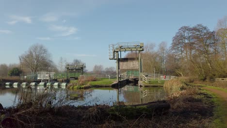 Toma-De-Izquierda-A-Derecha-De-La-Puerta-De-Bloqueo-Para-El-Agua-Del-Río-Traída-A-Este-Lago-En-Norfolk-Inglaterra-Y-Su-Hermosa-Vista-De-Fondo