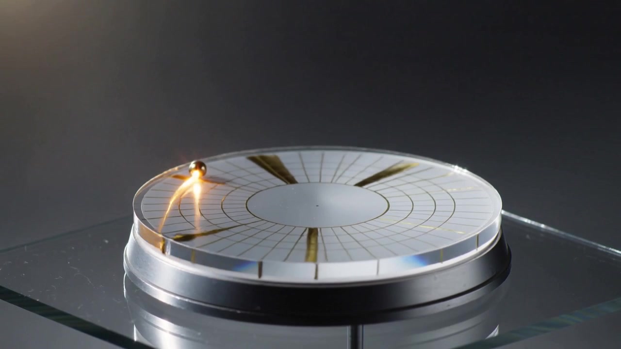 Starting showing metal ball rolling along groove on disc with gold radials at desk suggesting spark