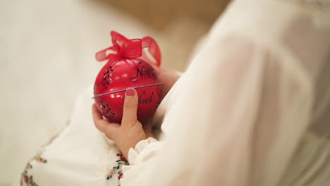 Sobre-El-Hombro-De-Un-Niño-Con-Un-Vestido-Blanco-Navideño-Sosteniendo-Un-Adorno-Rojo---Primer-Plano