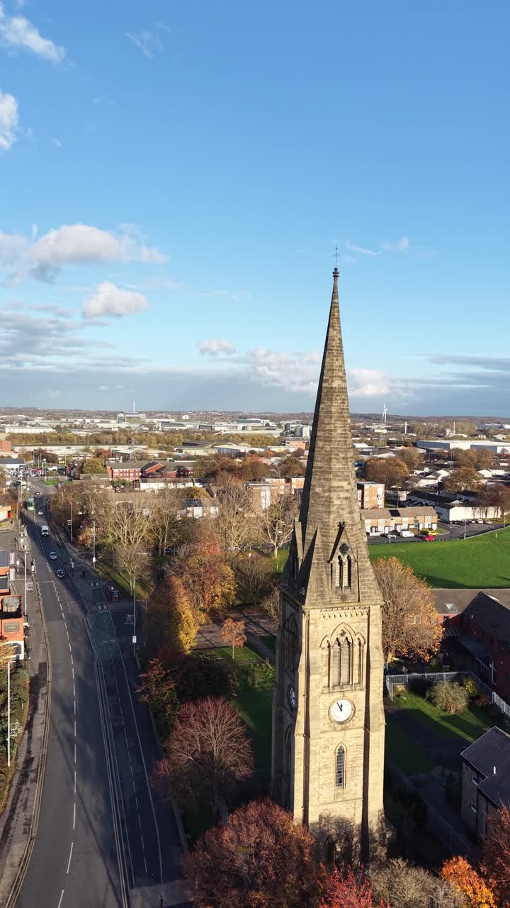 Vista drone verticale in stile social media di una storica guglia di chiesa a Hedge End, Hampshire, che sovrasta la città circostante, spazi verdi, alberi autunnali e cielo blu chiaro