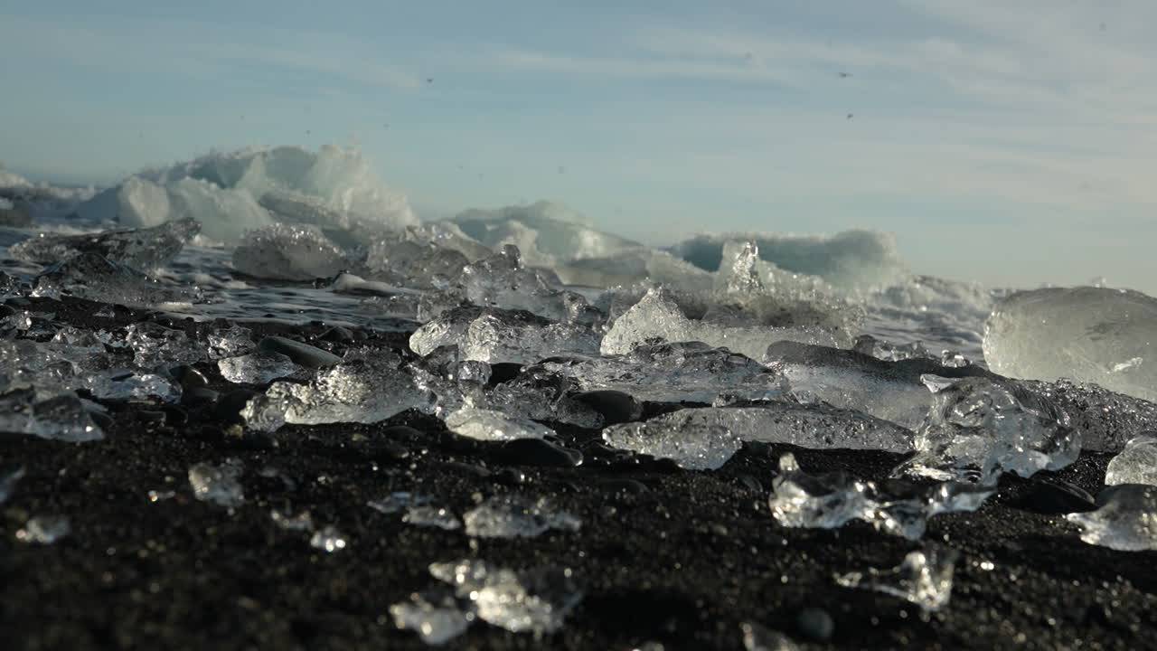 Small ice chunks scattered over dark sand, glistening under a clear sky on a cold beach