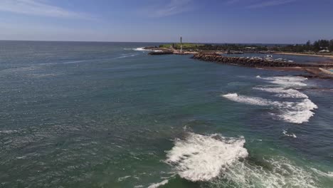 aerial reveal over the surf and rocks of wollongong harbour and the light houses