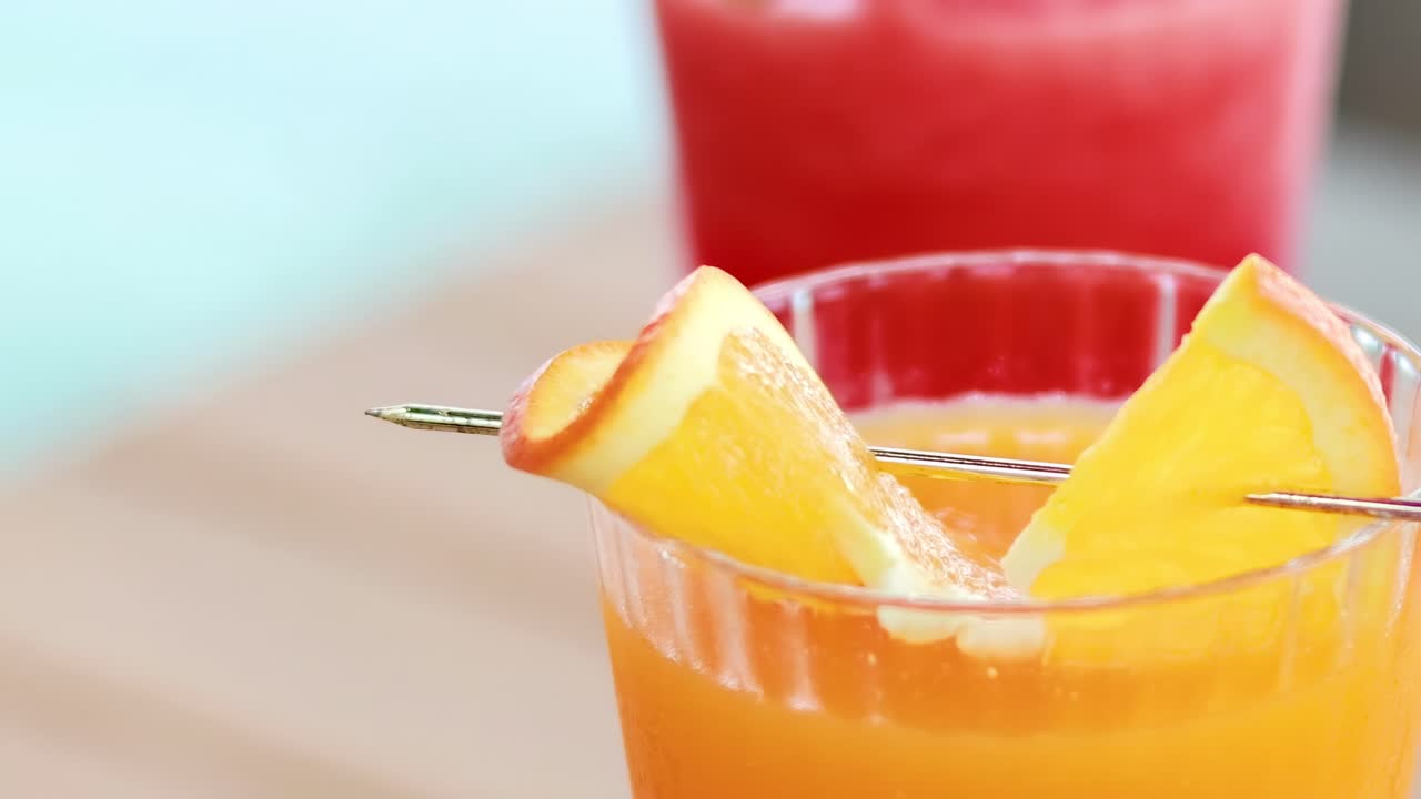 Close-up of orange and red juices with orange slices on a wooden table.