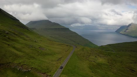 aerial view following car along stunning faroe islands coastal highland road