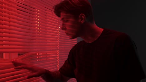 man looking through red lit blinds