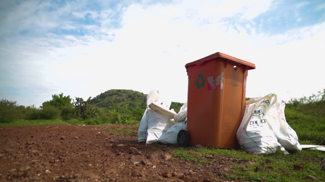 Ripresa cinematografica di sacchi della spazzatura raccolti e un bidone per la raccolta differenziata, durante una pulizia ambientale a Cerro del Piloncillo a Irapuato, che evidenzia sostenibilità, ecologia e azione comunitaria