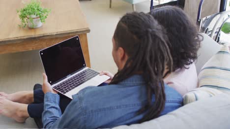 feliz pareja biracial sentada en el sofá usando una computadora portátil en la sala de estar, copia el espacio en la pantalla