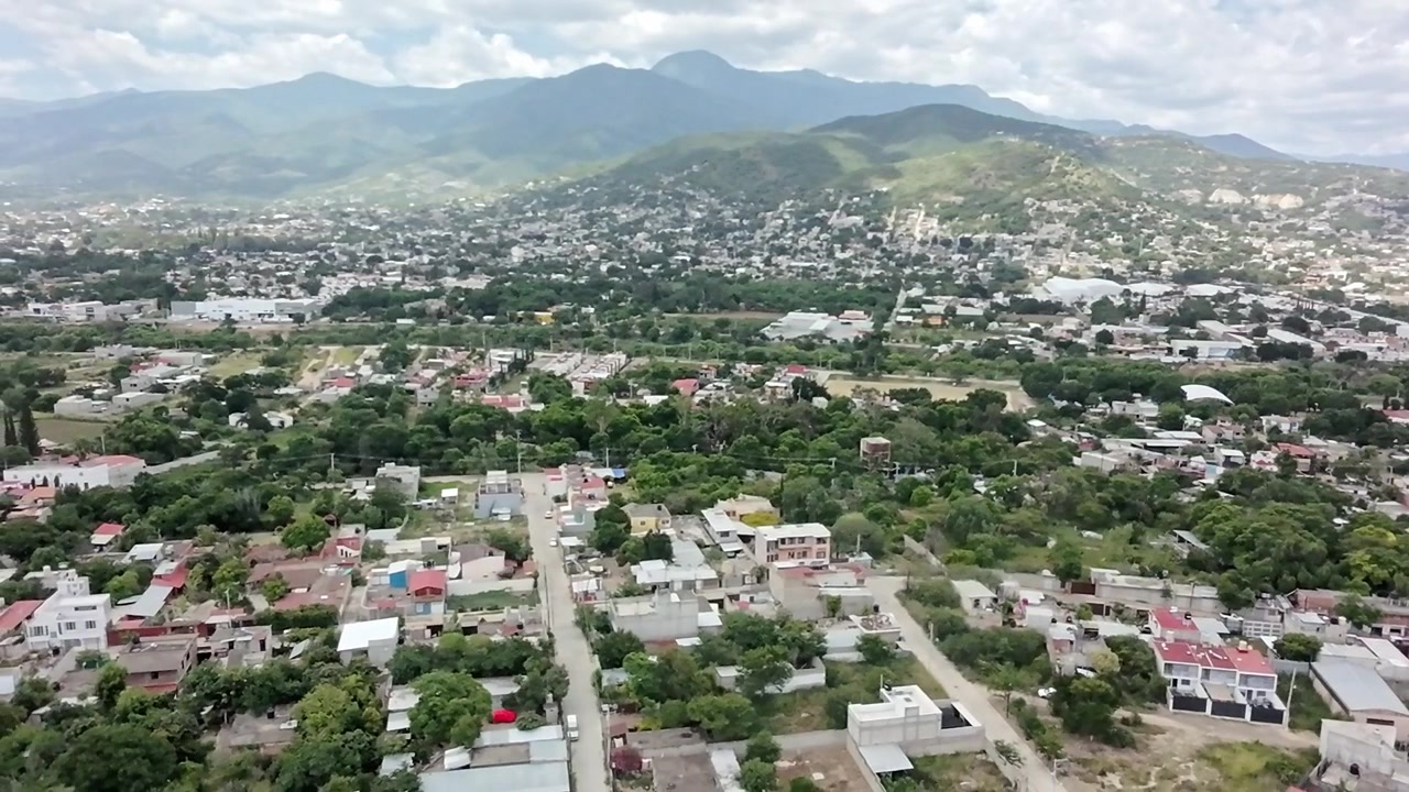 Vista aerea con drone della città di Huatulco con quartieri residenziali, vegetazione lussureggiante e montagne circostanti che evidenziano la crescita urbana e il paesaggio scenografico