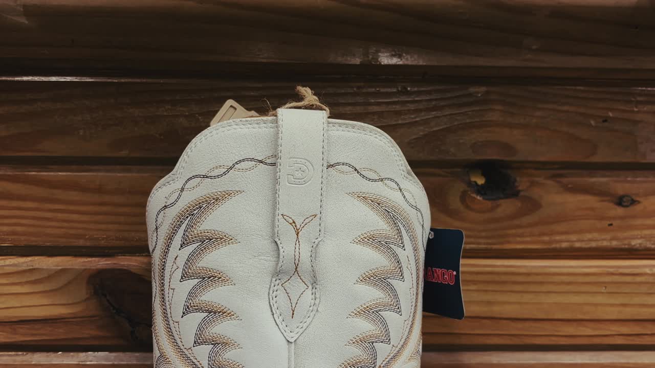 Vista detallada de una bota de cowboy blanca con bordados en una estantería de madera en Texas