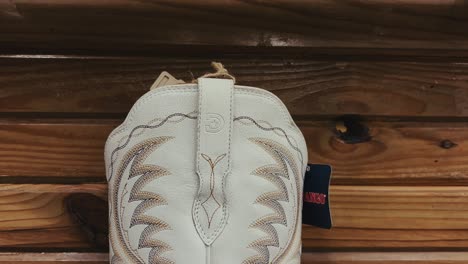 Vista detallada de una bota de cowboy blanca con bordados en una estantería de madera en Texas
