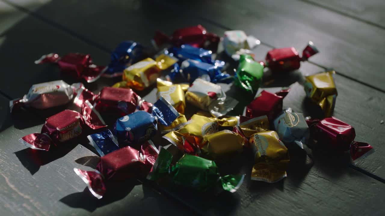 Framing assorted foil-wrapped candies resting on dark wooden tabletop, highlighting color contrast