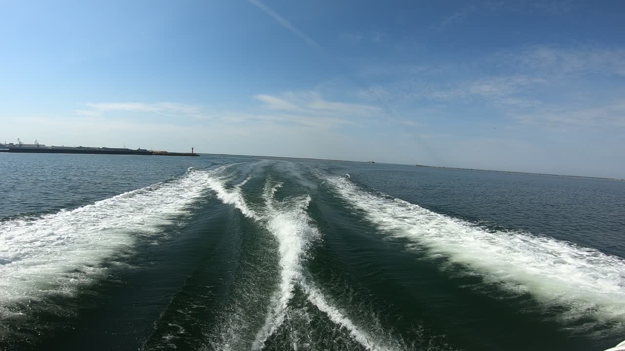A high-speed boat leaves a dynamic wake as it exits a coastal harbor into the open sea under a bright blue sky. Captures the thrill of marine travel, nature, and summertime freedom.
