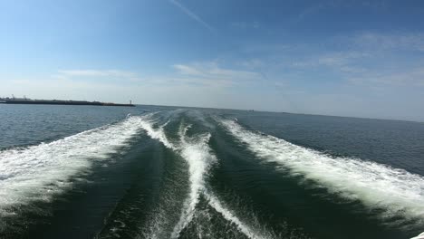 a high-speed boat leaves a dynamic wake as it exits a coastal harbor into the open sea under a bright blue sky. captures the thrill of marine travel, nature, and summertime freedom.