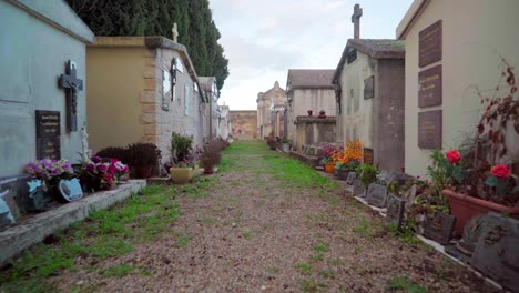 Walking-through-a-cemetery-alley,-quiet-and-empty-graveyard,-with-tombs,-graves-and-flowers-on-a-sunny-day