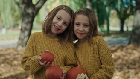 twins standing with small pumpkins at halloween.