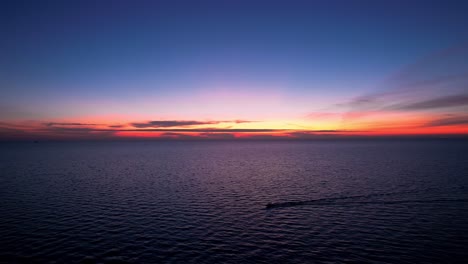 Drohnensilhouette-Eines-Schnellboots,-Das-Morgens-Mit-Einem-Farbenfrohen-Sonnenaufgang-über-Das-Meer-Rast