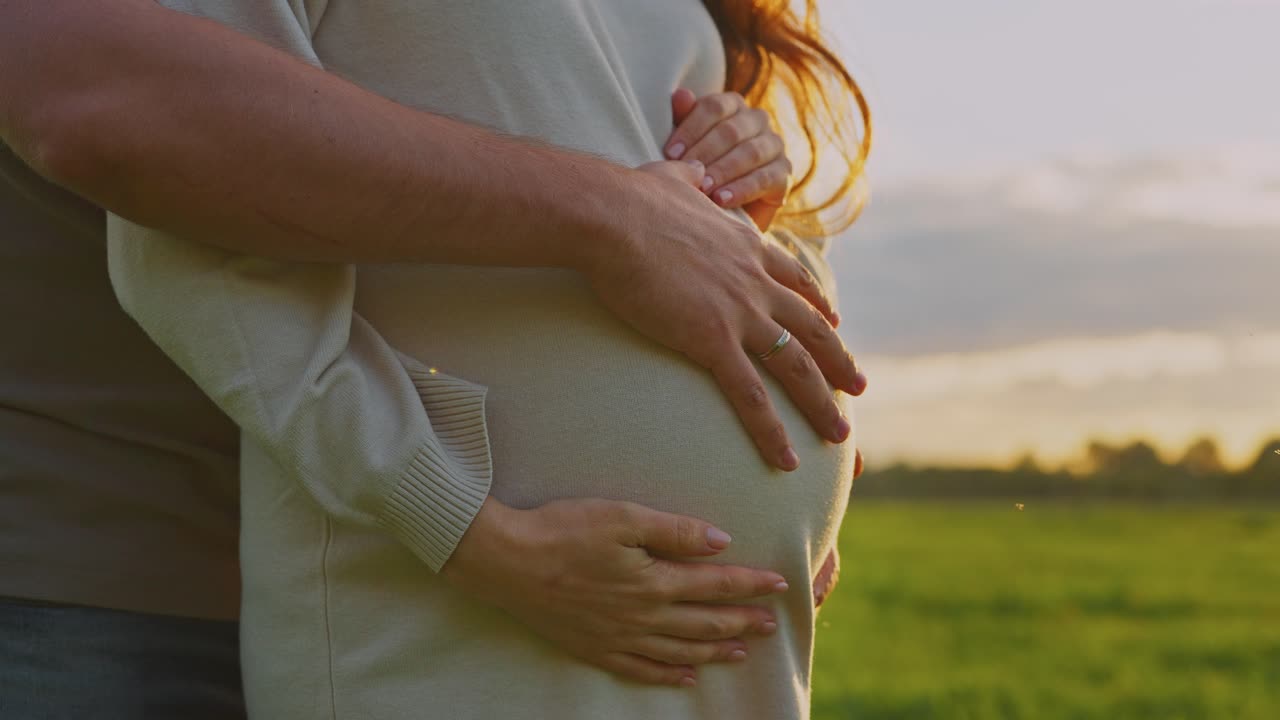 Et kjærlig par omfavner en gravid kvinne på et jorde ved solnedgang