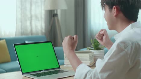 close up of asian man student celebrating while looking at green screen computer at home