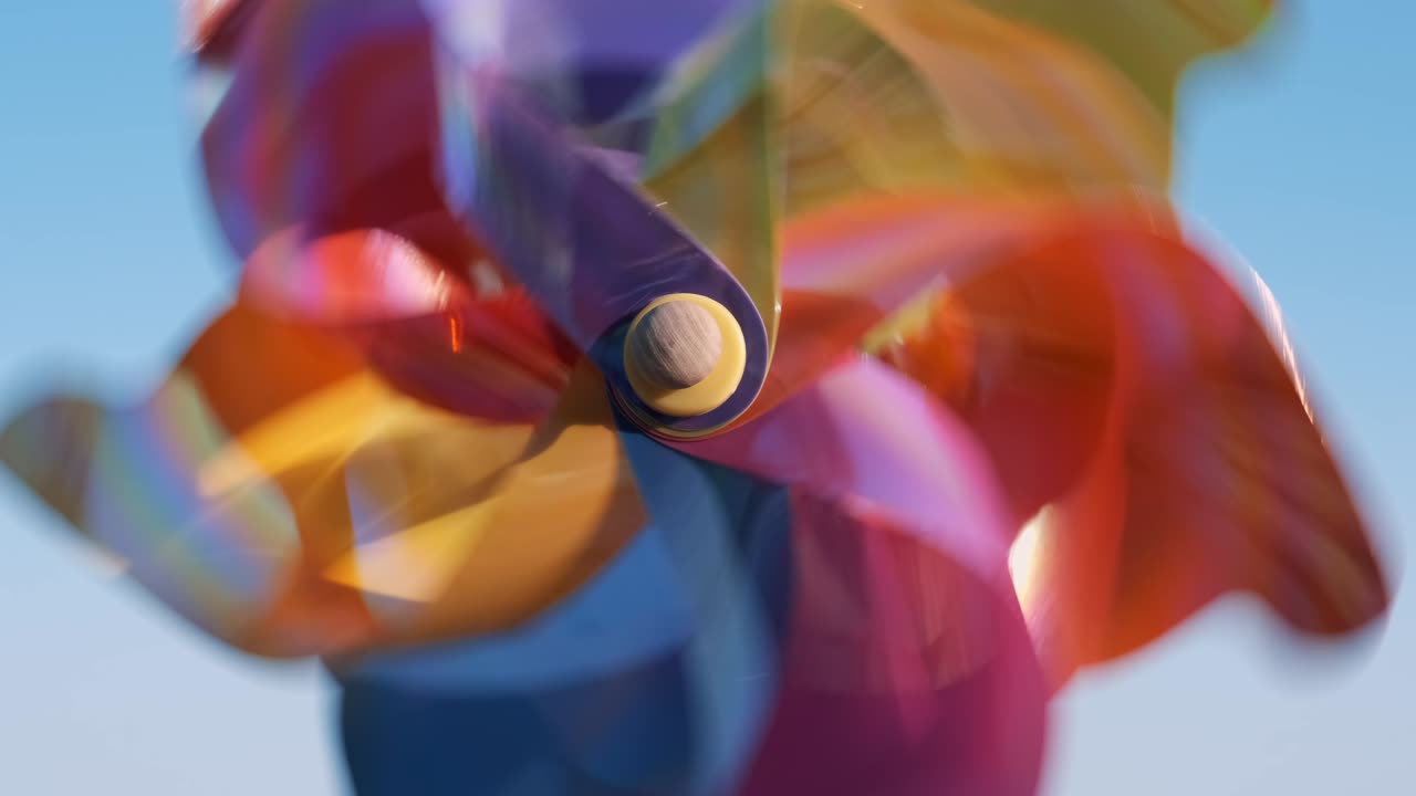 Rotating multi-colored plastic pinwheel with a blowing wind stands on the sand by the sea against the background of blue waves and the horizon with a blue sky. Toy mill on beach. Copyspace. Pattern