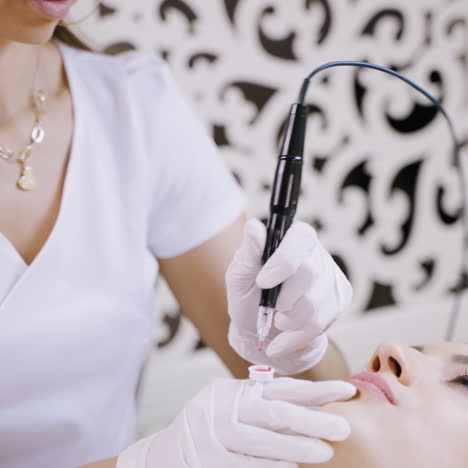 beautiful cosmetologist applying permanent make-up on lips in a beauty salon. close-up attractive beautician doing tattooing lips for a female patient.