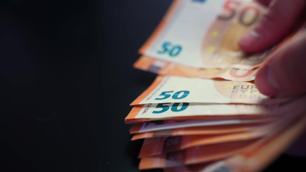 Una mano sventaglia una pila di banconote da 50 euro su un tavolo scuro con spazio per il testo, illustrando concetti di spesa in contanti, budgeting e pagamenti aziendali
